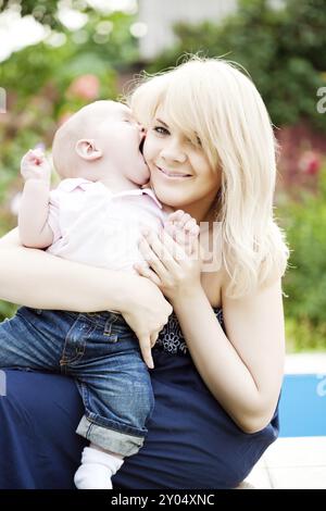 Heureuse jeune femme assise avec bébé garçon dans le jardin fleuri de printemps Banque D'Images