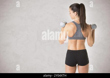 Close up de l'arrière d'un fit woman working out with dumbbells, isolé en gris Banque D'Images