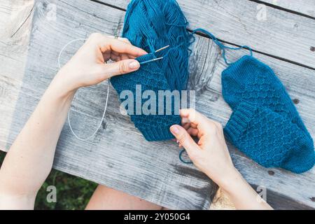 Femme tenant dans les mains le travail de tricot bleu sur fond en bois gris. Tricoter fille sur l'arrière-cour. Crochet à tricoter bleu dans les mains de fille sur la table en bois. Banque D'Images