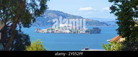 Grand téléobjectif panoramique du pénitencier fédéral d'Alcatraz et de l'île au milieu de la baie de San Francisco encadrée par des arbres de grand angle les jours ensoleillés Banque D'Images