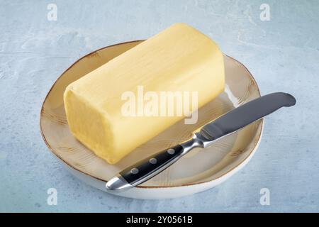 Un bloc de beurre avec un couteau sur une assiette, sur un fond d'ardoise, ingrédient de cuisson, produit laitier Banque D'Images