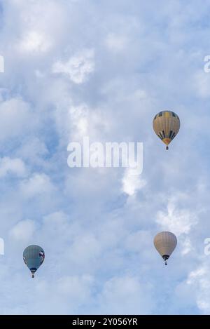 Trio de montgolfières vibrantes flotte à travers les nuages, participant à une compétition passionnante, mettant en vedette des designs colorés sur fond de cl Banque D'Images