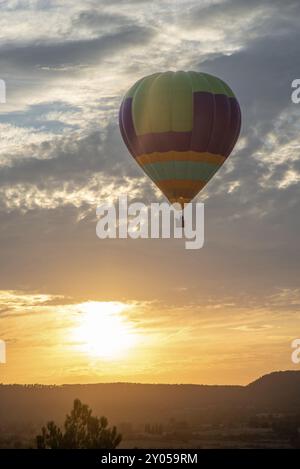 Une montgolfière dynamique prend le ciel au crépuscule, pilotée par des gens, sous un ciel couvert de nuages. La lumière du coucher de soleil crée un contraste saisissant avec Banque D'Images