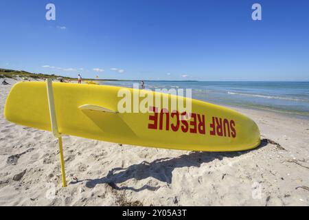Une planche de sauvetage jaune de surf repose sur une plage de sable près de l'océan par une journée ensoleillée avec un ciel bleu vif, Rorvig, Odsherred, Zealand, Danemark, Europe Banque D'Images