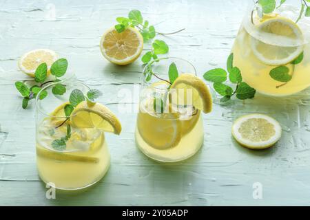 Limonade à la menthe. Boisson à l'eau de citron avec glace. Deux verres, un pichet et des citrons sur fond bleu. Boisson détox. Cocktail maison frais Banque D'Images