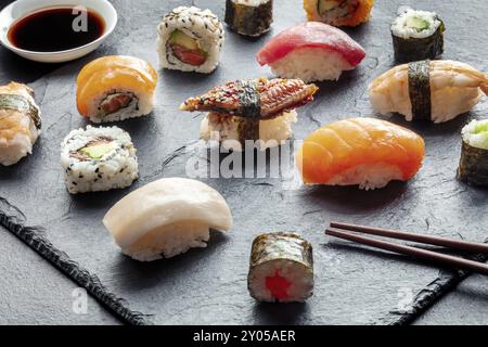 Sushi avec baguettes et sauce soja. Rouleaux, maki, nigiri sur fond noir, cuisine japonaise. Saumon, thon, anguille, crevettes et autres fruits de mer avec riz o Banque D'Images