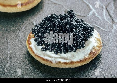 Un blini au caviar et au fromage à la crème, un gros plan sur un fond d'ardoise noire Banque D'Images