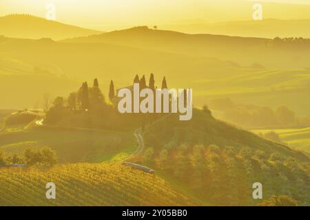 Une belle scène de campagne avec des collines ondulantes baignées de lumière dorée du matin, avec une ferme entourée d'arbres et une atmosphère brumeuse, San Banque D'Images