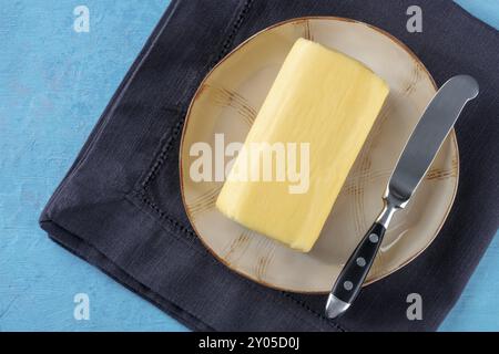 Un bloc de beurre avec un couteau sur une assiette, photographié d'en haut sur un fond bleu Banque D'Images