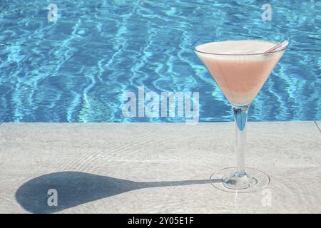 Verre élégant avec mousse blanche rose cocktail et tube sur la piscine rocheuse avec eau turquoise sur fond Banque D'Images