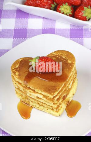 Pile de crêpes en forme de coeur avec sirop et une fraise sur un plat blanc avec fourchette. Un petit déjeuner parfait pour la Saint-Valentin Banque D'Images