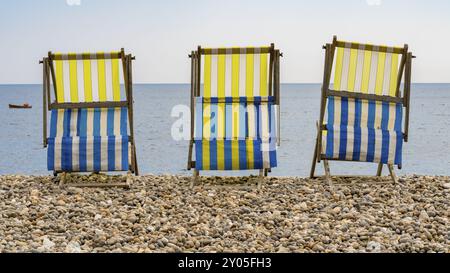 Empty Deck chaises sur la plage de galets à Beer, Devon, Royaume-Uni, regardant la baie de Seaton et la Manche britannique avec un petit bateau de pêche qui passe Banque D'Images