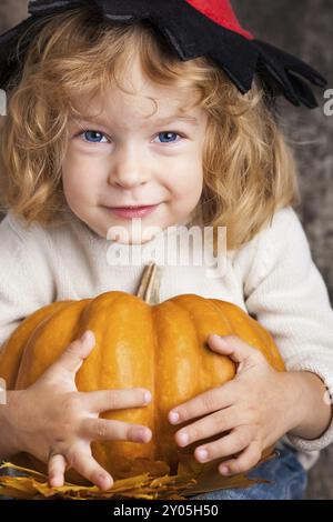 Heureux enfant souriant dans le chapeau de sorcière tenant une grande citrouille orange. Concept d'Halloween Banque D'Images