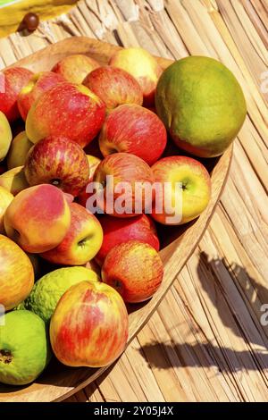 Bol en bois et matelas de paille rustique avec des goyaves, mangues, pommes et bananes sous les rayons du soleil Banque D'Images