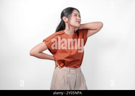 Jeune femme asiatique fatiguée dans une chemise brune souffrant de douleur, spasme musculaire sur le fond blanc isolé du cou. Banque D'Images