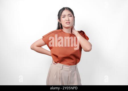 Jeune femme asiatique fatiguée dans une chemise brune souffrant de douleur, spasme musculaire sur le fond blanc isolé du cou. Banque D'Images