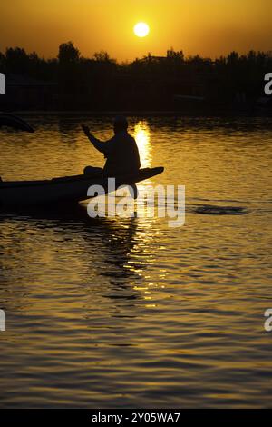 Un batelier cachemirien navigue son bateau lors d'un beau coucher de soleil sur le lac Dal, une destination touristique majeure à Srinagar, Cachemire, Inde, Asie Banque D'Images