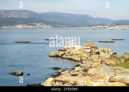 Rias Baixas Seascape avec phare Punta Cabalo et bateau à moules naviguant entre les lits de moules appelés bateas. Galice, Espagne, Europe Banque D'Images