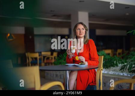 Fille en robe rouge buvant du café latte. Banque D'Images