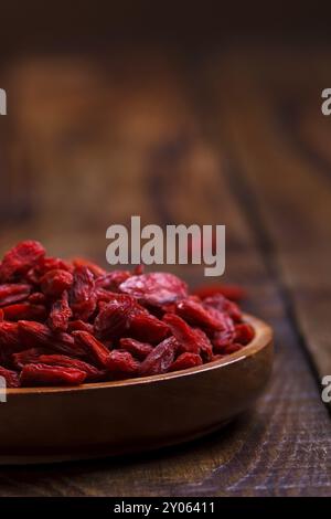 Baies de Goji dans un bol en bois sur une vieille planche rustique, mise au point sélective, macro Banque D'Images