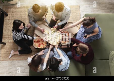 Une fête de pizza, un groupe d'amis discutant et mangeant joyeusement de la pizza à la table et buvant de l'eau gazeuse sucrée. Vue de dessus depuis le deuxième étage. Banque D'Images