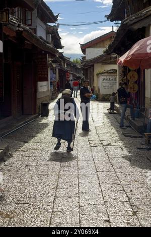 Lijiang, Chine, 21 septembre 2007 : une femme mature de la minorité ethnique naxi marchant dans une ruelle préservée avec des bâtiments traditionnels chinois dans l'ancien Lijiang Banque D'Images