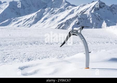 Gros plan d'une hache glacée dans la neige avec des montagnes enneigées en arrière-plan Banque D'Images