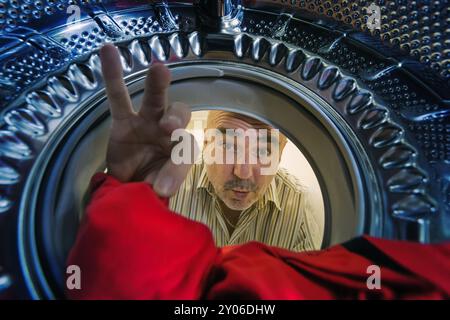 Un homme regarde dans la machine à laver et attrape un chiffon rouge Banque D'Images