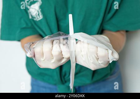 Femme médecin dans les vêtements de plaine ouvrant l'emballage médical. Gros plan des mains féminines avec des gants blancs ouvrant l'emballage. Banque D'Images