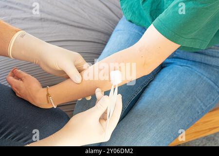 Docteur en vêtements de plaine traitant le bras d'une femme. Soins à domicile pour une fille. Médecin sans manteau blanc avec des gants blancs donnant des soins médicaux à domicile. Banque D'Images