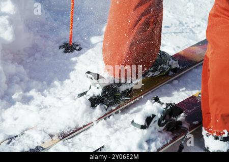 Chaussures de ski alpin orange dans une monture de ski. Une chaussure est complètement fixée sur les skis, la seconde ne l'est pas. Gros plan. Costume orange Banque D'Images