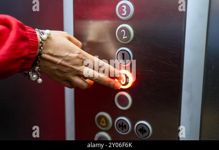 Femme en robe rouge appuyant sur le bouton à l'intérieur de l'ascenseur. Banque D'Images