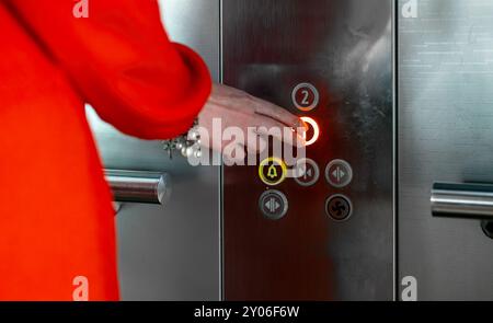 Femme en robe rouge appuyant sur le bouton à l'intérieur de l'ascenseur. Banque D'Images