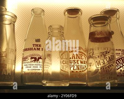 Sélection de bouteilles de lait en verre vintage portant le nom ou les noms de produits laitiers ou de laiteries, rétro-éclairé dans la vitrine. Thèmes : livraison de lait, rond de lait. Banque D'Images