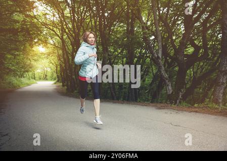 Une jeune femme blonde qui court s'exerce à l'extérieur dans un parc de montagne de la ville dans la forêt. Rayons chauds à travers les branches des arbres Banque D'Images