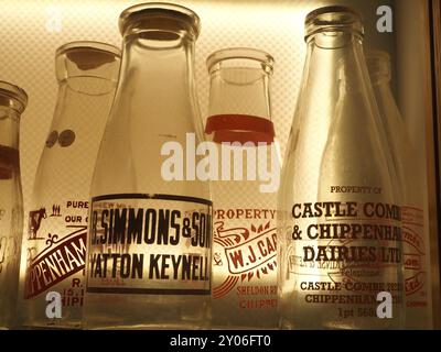 Sélection de bouteilles de lait en verre vintage portant le nom ou les noms de produits laitiers ou de laiteries, rétro-éclairé dans la vitrine. Thèmes : livraison de lait, rond de lait. Banque D'Images