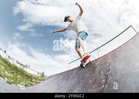 Adolescent patineur raccroché au-dessus d'une rampe sur une planche à roulettes dans un skate Park. Grand angle Banque D'Images