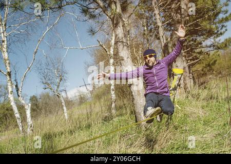 Un homme à l'âge de s'asseoir sur slackline, de prendre l'équilibre et de profiter de la vie Banque D'Images