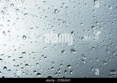 Fond texturé de vitres de fenêtre avec un fond nuageux. Motif naturel d'une goutte de pluie sur un fond nuageux Banque D'Images