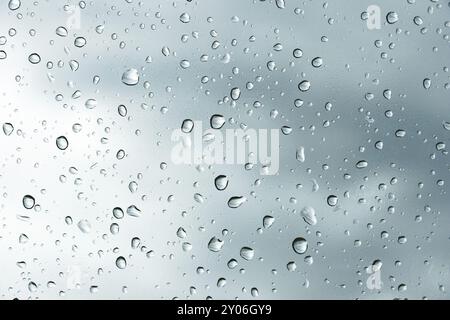 Fond texturé de vitres de fenêtre avec un fond nuageux. Motif naturel d'une goutte de pluie sur un fond nuageux Banque D'Images