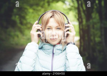 Portrait d'une fille de sport attrayante blonde dans une veste de descente légère habillant casque bluetooth avec de la musique ou les sons de la nature tout en étant sur Banque D'Images