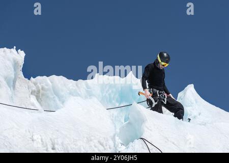 Un alpiniste professionnel portant un casque et un masque de ski sur l'assurance entaille la hache de glace dans le glacier. Le travail d'un grimpeur professionnel en Winte Banque D'Images