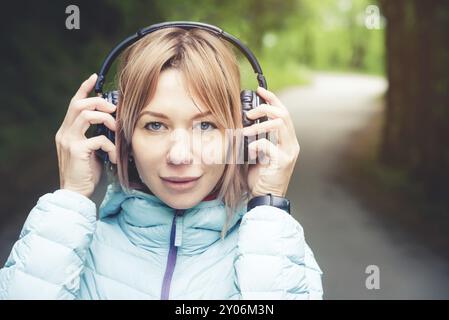 Portrait d'une fille de sport attrayante blonde dans une veste de descente légère habillant casque bluetooth avec de la musique ou les sons de la nature tout en étant sur Banque D'Images