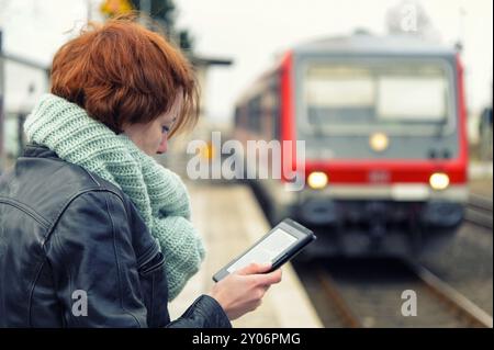 Jeune femme lisant un eBook sur le quai à l'arrivée du train Banque D'Images