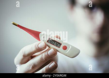 L'homme est titulaire d'un thermomètre rouge avec une température élevée à la main, visage floue Banque D'Images