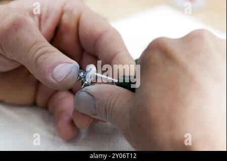 Mains d'un technicien dentaire avec meuleuse et couronnes métalliques Banque D'Images