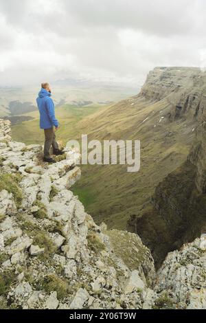 Touriste hipster barbu debout sur le bord d'un rocher et regardant au loin sur un plateau épique. Le concept de tourisme Banque D'Images