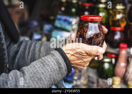 Les vieilles mains féminines ridées tiennent un pot avec de la confiture maison faite de cônes dans les montagnes Banque D'Images