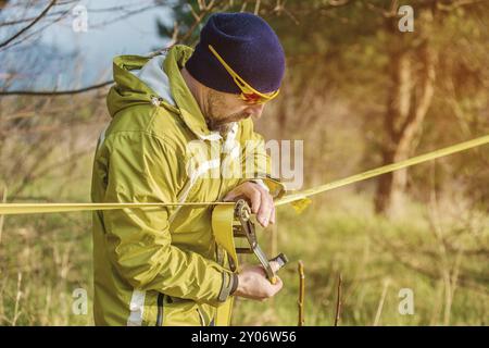 Gros plan Un homme ajuste le slackline de l'équipement avant d'effectuer des tours de slackline fous et de marcher sur un slacklin dans un parc dans la nature Banque D'Images