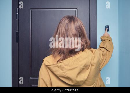 Personne en veste jaune sonnant la sonnette. Photographie vue arrière d'une personne appuyant sur un bouton de sonnette à côté d'une porte en bois sombre dans un cadre intérieur Banque D'Images